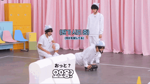 a man wearing a cat ear helmet is crawling on the floor in front of a pink curtain
