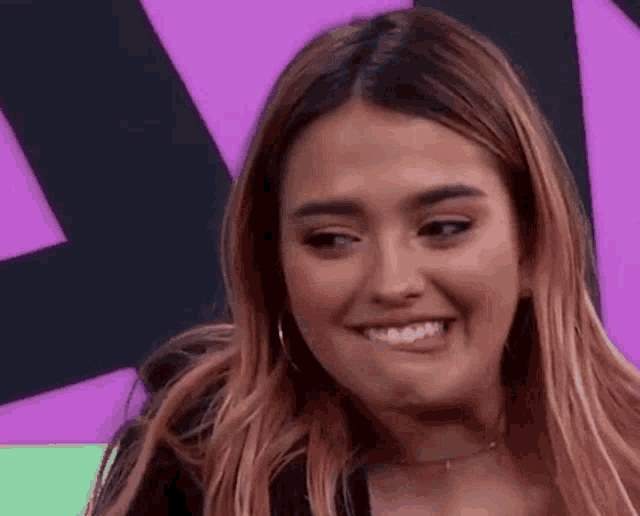 a woman with long hair is smiling and making a funny face in front of a purple background .