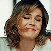 a woman with short hair is smiling with her eyes closed and her hair blowing in the wind .
