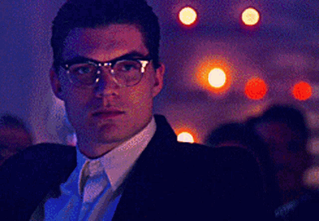 a man wearing glasses and a suit looks at something