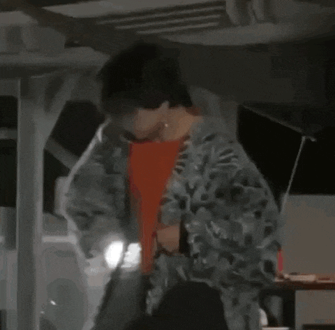 a man in a camouflage jacket is standing in front of a car at night .