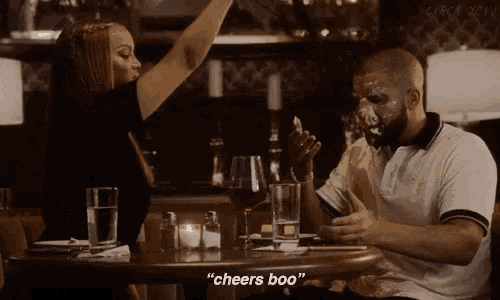 a man and a woman are sitting at a table and a woman says cheers boo