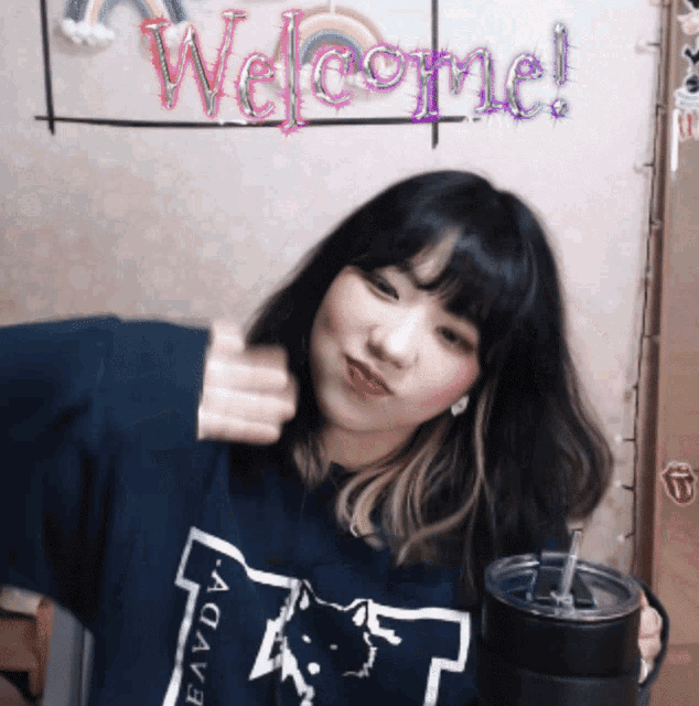 a girl in a blue shirt is standing in front of a wall with welcome written on it