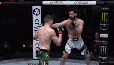 two men are fighting in a cage with a monster energy drink in the background
