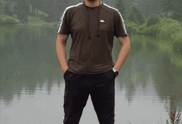 a man wearing a kappa t-shirt stands in front of a lake