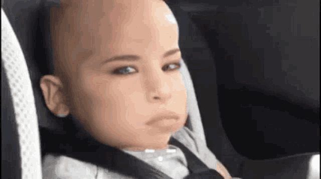 a baby with a bald head is sitting in a car seat .