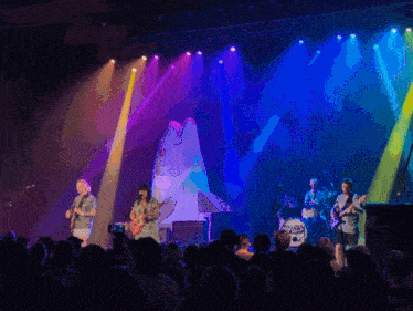 a group of people playing instruments on a stage with a fish on the wall behind them
