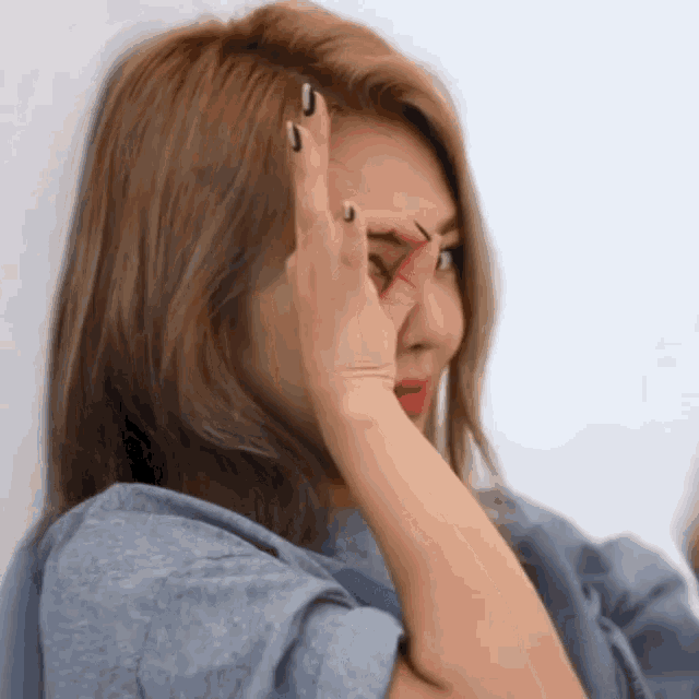 a woman covering her face with her hand while wearing a gray shirt