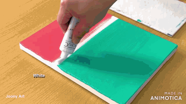 a person is applying white paint to a red and green canvas