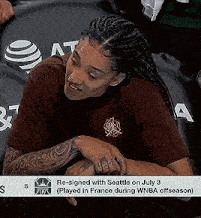 a woman with braids and tattoos is sitting on a couch with her head on her arms .