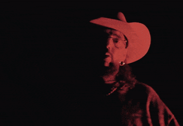 a man with a beard wearing a cowboy hat in a dark room