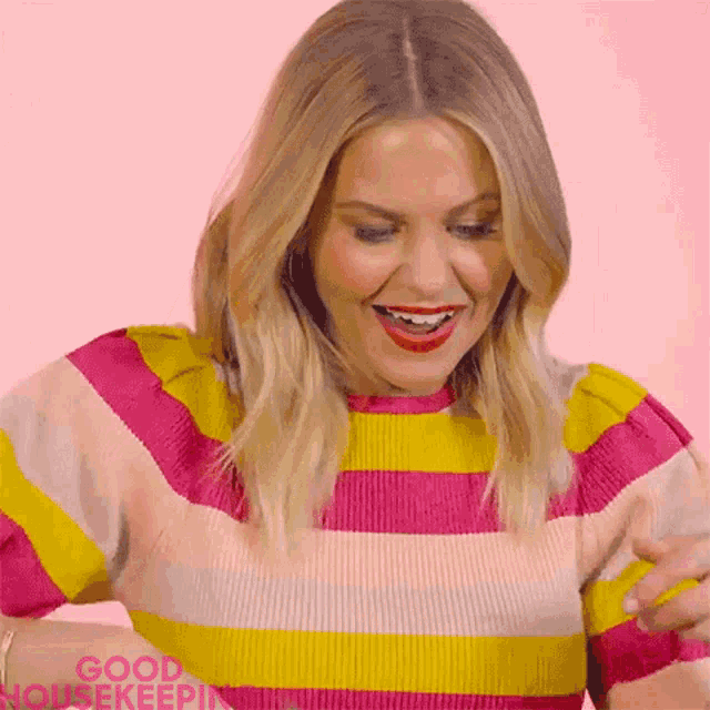 a woman in a pink and yellow striped sweater is smiling and looking down .