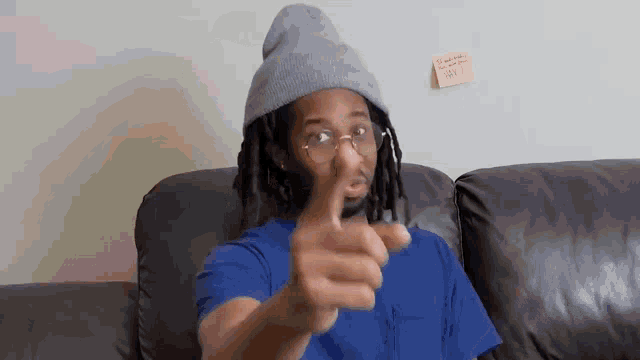 a man with dreadlocks is sitting on a couch giving a thumbs up sign .