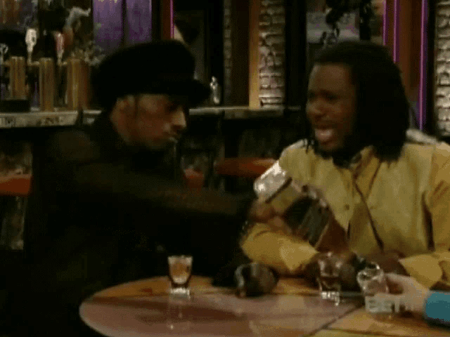 two men are sitting at a table and one is pouring a drink into a shot glass