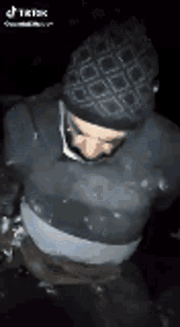 a man wearing a beanie and a sweater is standing in a dark room .