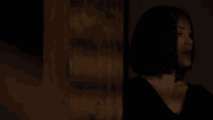 a woman wearing a black shirt and a necklace stands in a dark room