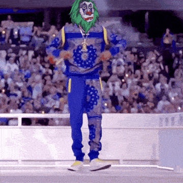 a clown with a green beard is dancing on a stage in front of a crowd