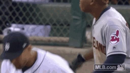 two baseball players are standing next to each other on the field . one of the players is wearing an indians jersey .