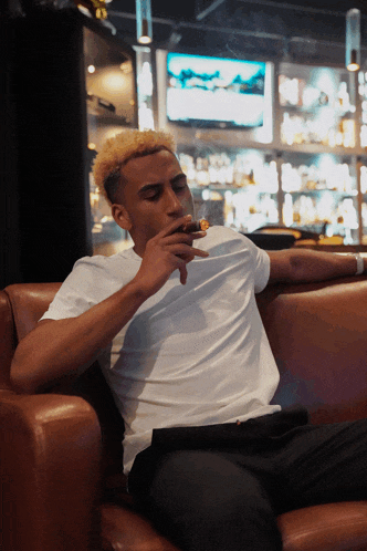 a man in a white shirt is sitting on a couch smoking a cigar