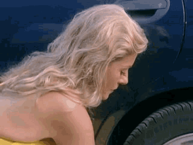 a woman in a yellow dress is kneeling down next to a car .