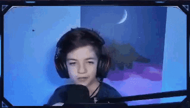 a young boy wearing headphones and a microphone is sitting in front of a screen .