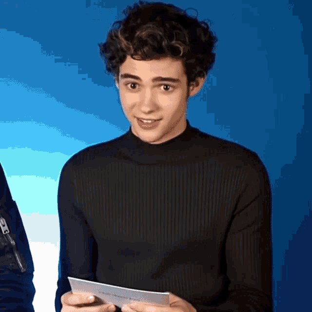 a young man with curly hair is holding a piece of paper in his hands .