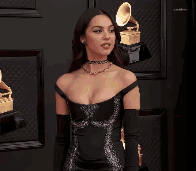 a woman in a black dress and gloves is standing in front of a wall with trophies on it