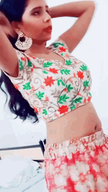a woman in a floral crop top and red skirt is standing with her hands behind her head