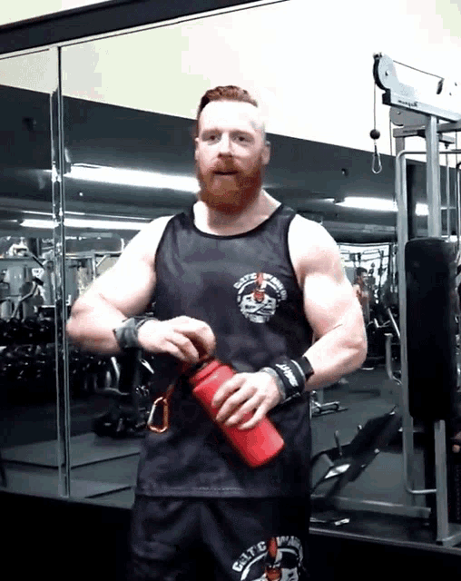 a man with a beard wearing a black tank top that says ' elite ' on the front