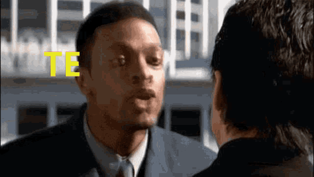 a man in a suit and tie is talking to another man in front of a building with the word te on the screen