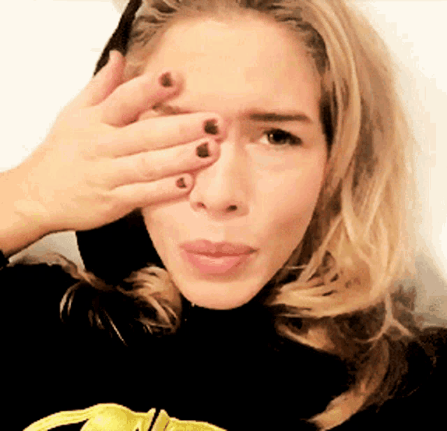 a woman covering her face with her hand while wearing a black shirt with a yellow bow on it