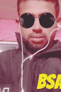 a man wearing sunglasses and ear buds has a bsa logo on his jacket