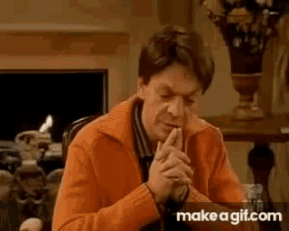 a man in an orange sweater is praying with his hands folded .