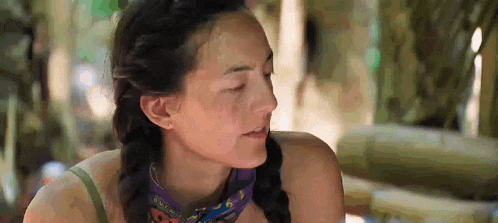 a woman with braids and a bandana around her neck is sitting in the jungle .