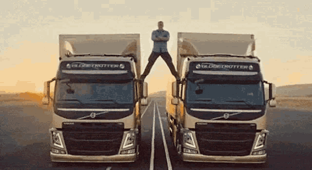 a man is standing on the back of two trucks .