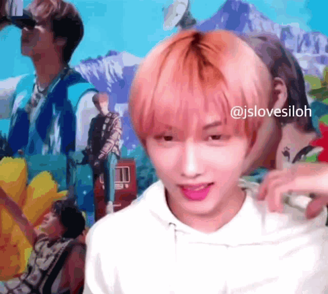 a young man with pink hair is standing in front of a wall with pictures of boys .