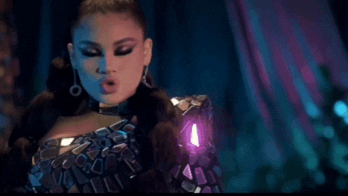a woman in a purple dress and earrings is standing in a dark room and looking at the camera .