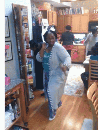 a woman in a robe is dancing in a kitchen with other people