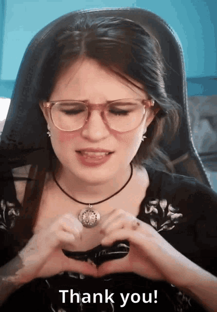 a woman wearing glasses and a necklace making a heart shape with her hands and the words thank you behind her