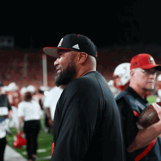 a man wearing a black adidas hat stands on a football field