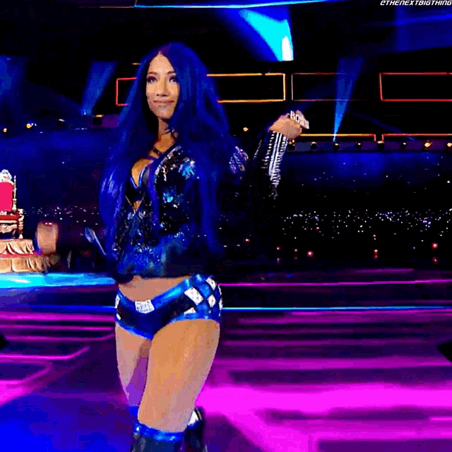 a woman with blue hair is dancing on a stage in front of a crowd