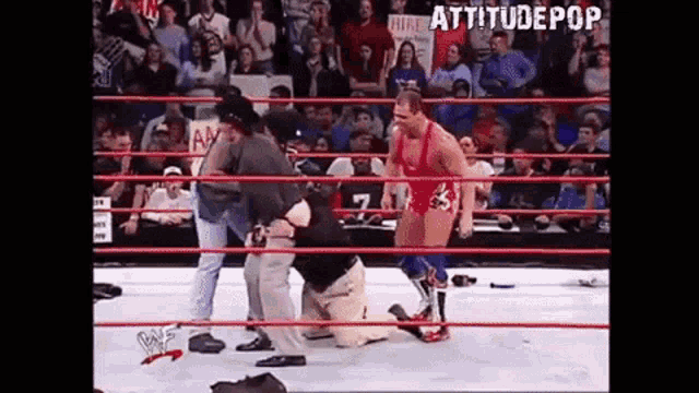 a wrestler is kneeling down in a wrestling ring while a referee stands behind him .