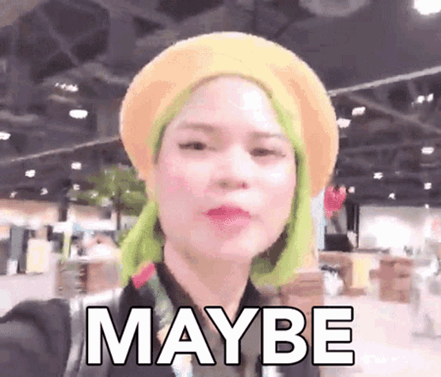 a woman with green hair is wearing a beret and making a funny face with the word maybe .