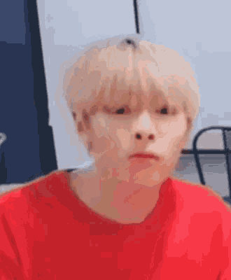 a young man with blonde hair is wearing a red shirt and making a funny face