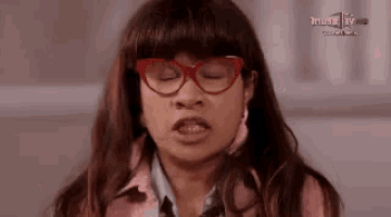 a woman wearing red glasses and a pink shirt is making a funny face .