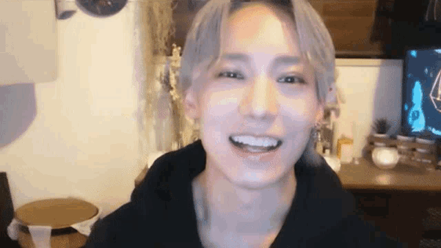 a young man with gray hair is smiling and looking at the camera while wearing a black hoodie .