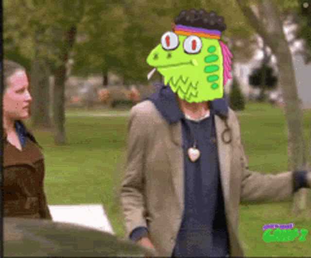 a man with a cartoon face on his head stands in a park