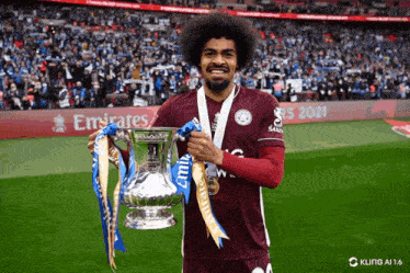 a soccer player is holding a trophy in front of an emirates banner