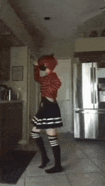 a girl with red hair is dancing in front of a stainless steel refrigerator