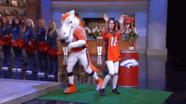 a woman in a broncos jersey stands next to a mascot on a stage